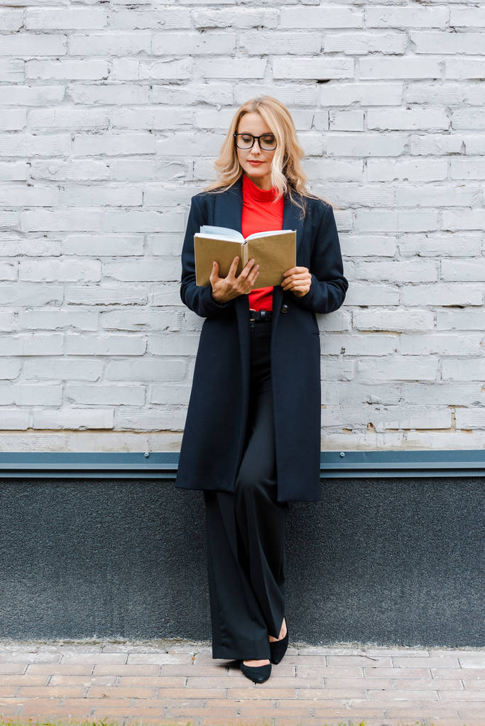 ελκυστική επιχειρηματίας σε μαύρο παλτό και γυαλιά βιβλίο ανάγνωσης  - Φωτογραφία, εικόνα
