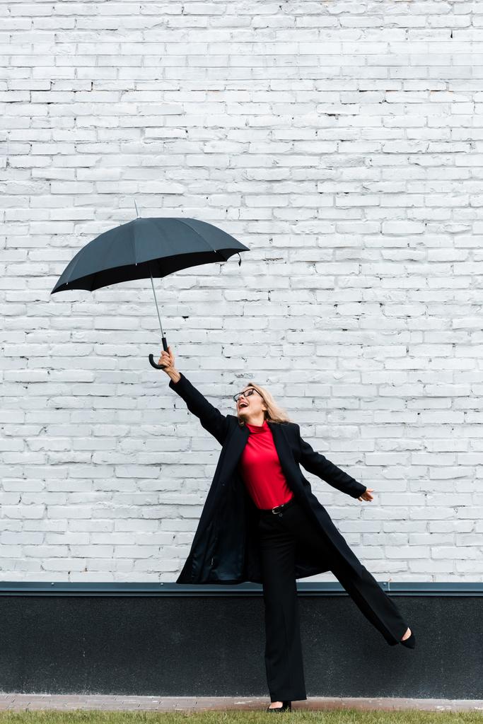 Siyah ceketli, gülümseyen ve şemsiyesi olan çekici bir iş kadını.  - Fotoğraf, Görsel