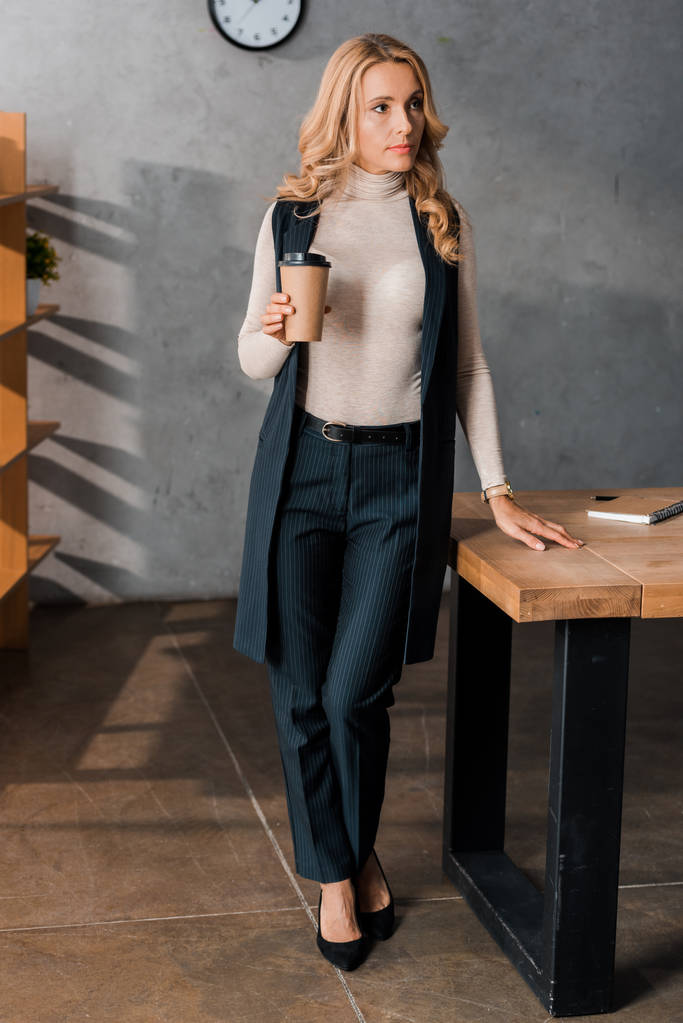 atrakcyjne i blondynka bizneswoman trzyma papierowy kubek w biurze  - Zdjęcie, obraz