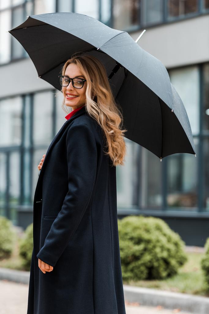 attraente e sorridente donna d'affari in cappotto nero con ombrello
  - Foto, immagini