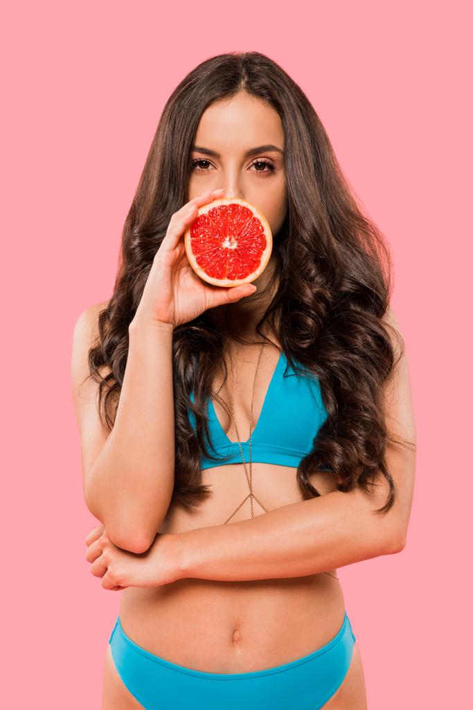 woman in swimsuit covering face with half of grapefruit isolated on pink  - Photo, Image