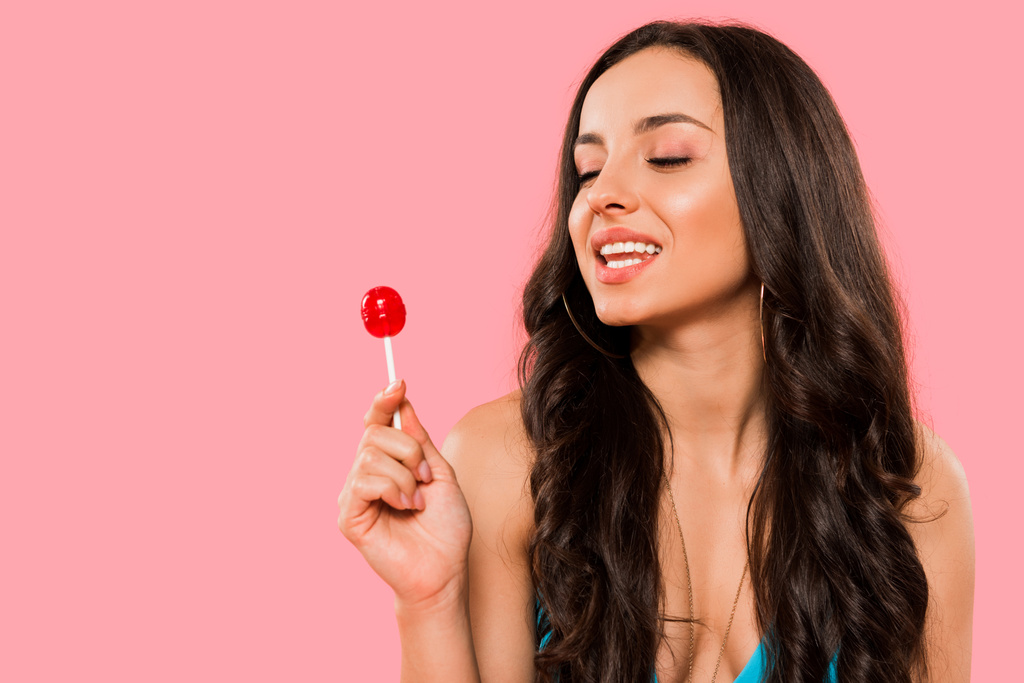 attractive girl looking at sweet lollipop isolated on pink  - 写真・画像