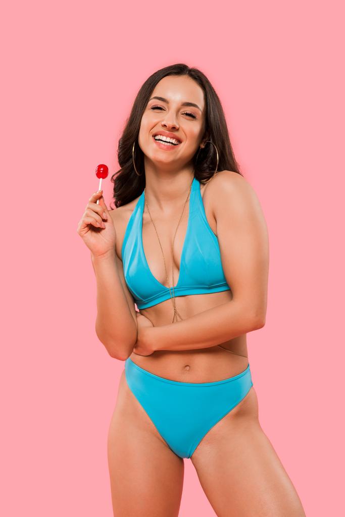 happy woman in swimsuit holding sweet lollipop isolated on pink  - 写真・画像