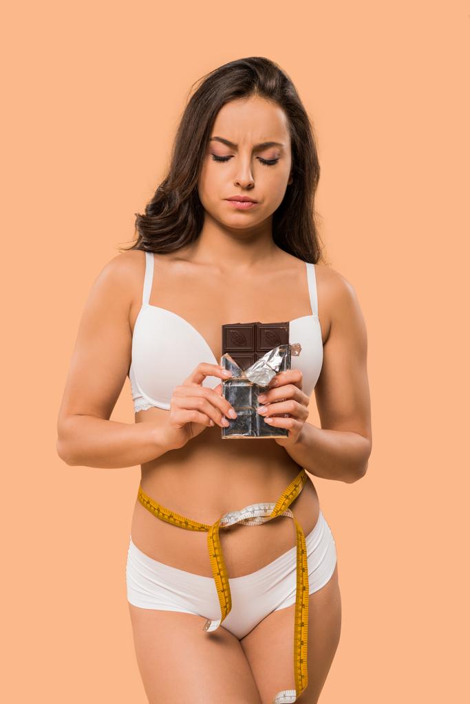 atraktivní žena s měřicí páskou drží čokoládovou tyčinku izolovanou na béžové  - Fotografie, Obrázek