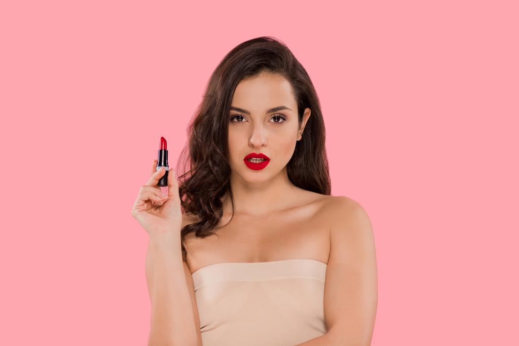 attraktive Frau mit roten Lippen hält Lippenstift isoliert auf rosa  - Foto, Bild