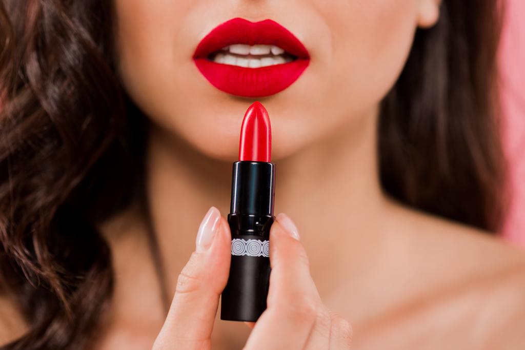 cropped view of woman holding lipstick near red lips isolated on pink  - 写真・画像