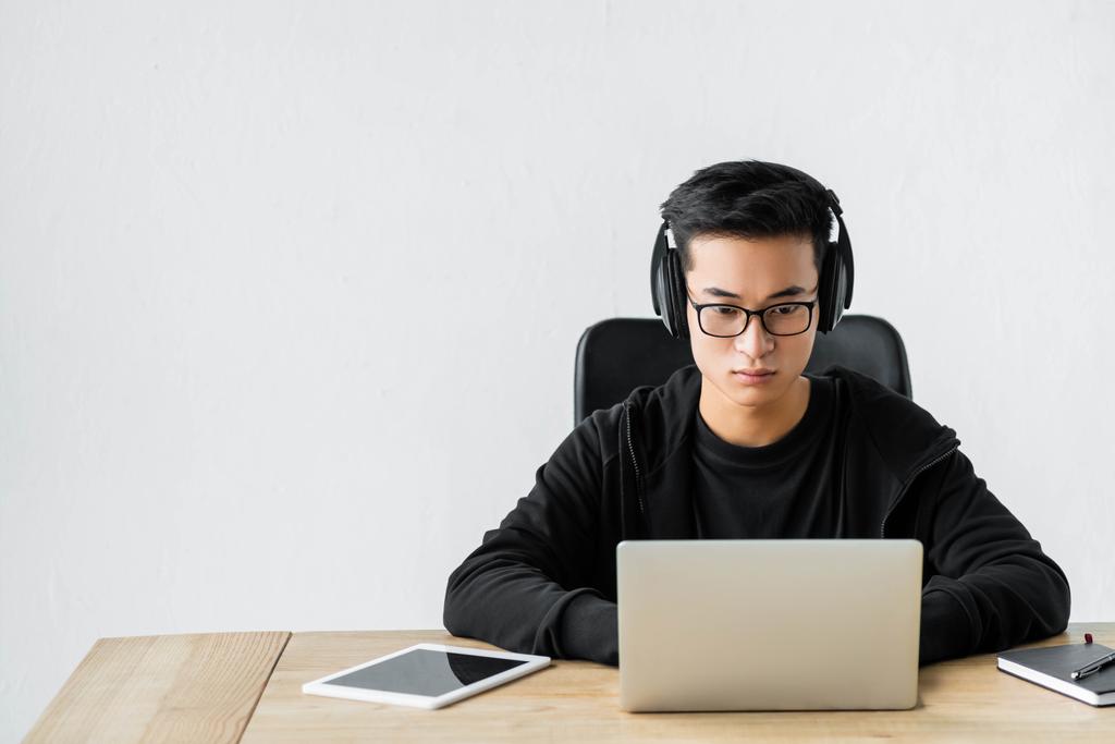 hacker asiático en los auriculares usando el ordenador portátil y sentado en la mesa
  - Foto, Imagen