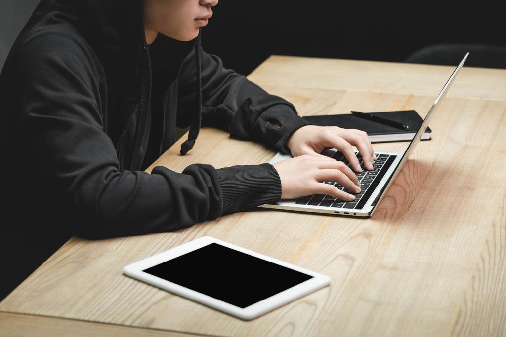 vista ritagliata di hacker utilizzando laptop e seduto a tavola
  - Foto, immagini