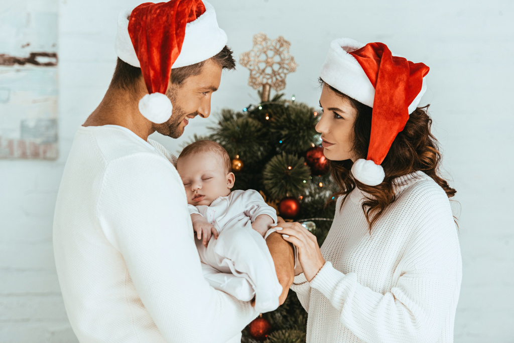 boldog nő nézi mosolygós férj kezében kislánya közel karácsonyfa - Fotó, kép