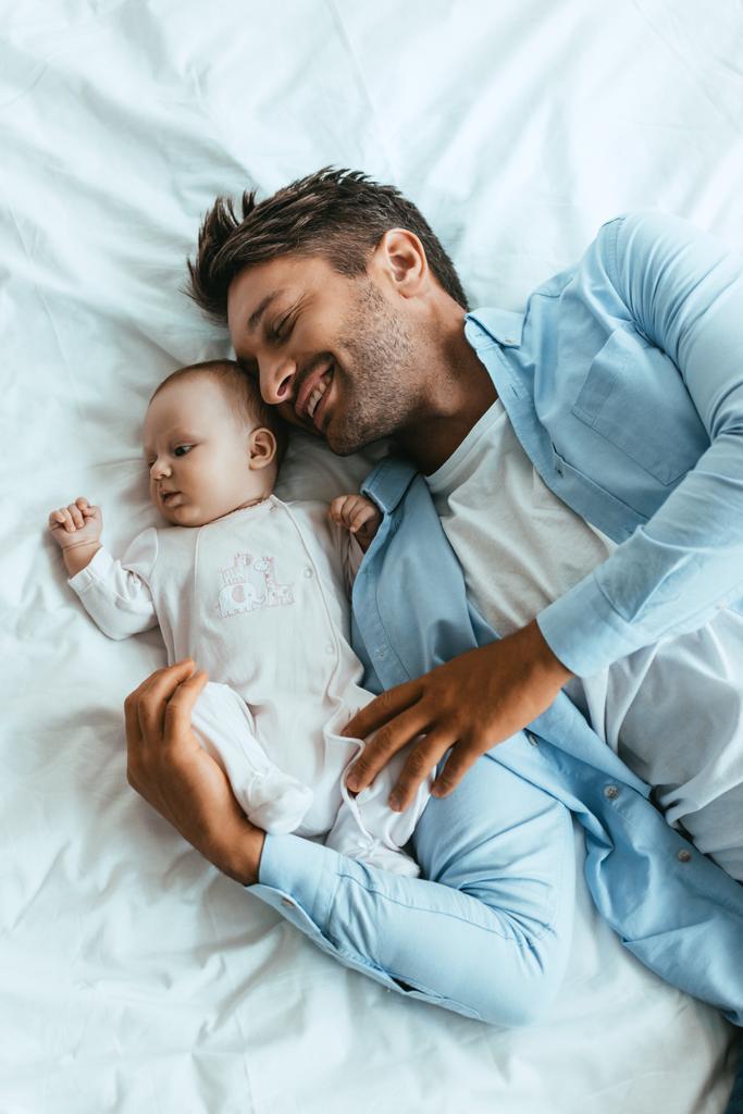 vue de dessus du père heureux étreignant bébé adorable tout en étant couché sur la literie blanche
 - Photo, image