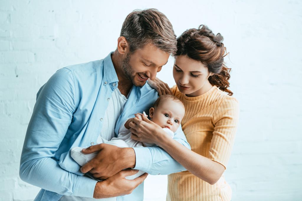 atractiva mujer de pie cerca feliz marido sosteniendo pequeño niño
 - Foto, Imagen