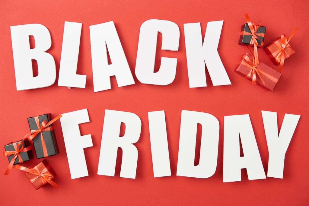 top view of black friday white lettering near small presents on red background - Photo, Image
