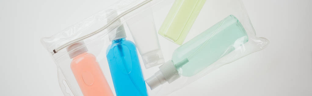 panoramisch shot van cosmetische tas met kleurrijke flessen met vloeistoffen op witte achtergrond  - Foto, afbeelding