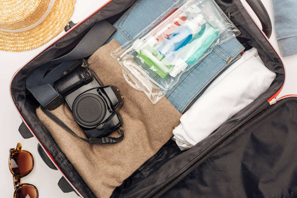 top view τσάντα ταξιδιού με πετσέτα, καλλυντικά τσάντα με πολύχρωμα μπουκάλια, ψηφιακή φωτογραφική μηχανή, ρούχα  - Φωτογραφία, εικόνα