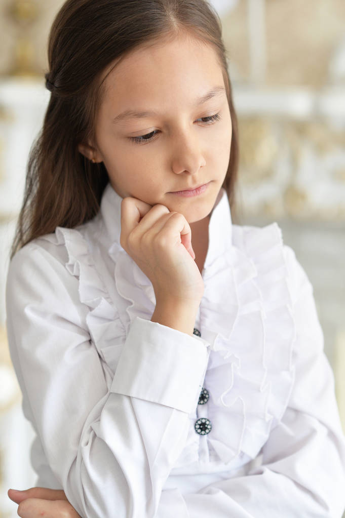 Surullinen pieni tyttö valkoisessa puserossa poseeraa kotona
  - Valokuva, kuva