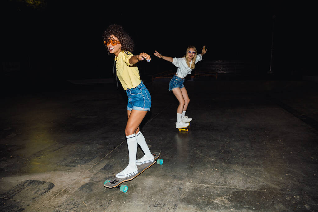Afbeelding van twee multinationale meisjes die glimlachen en skateboarden  - Foto, afbeelding