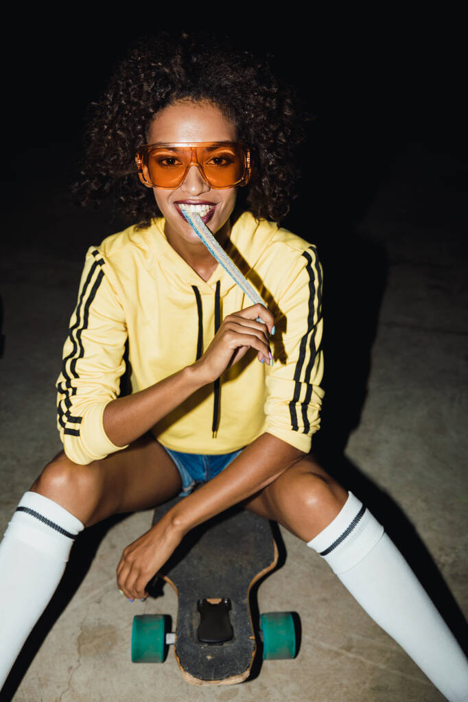 スケートボードで長いキャンディーを食べるアフリカ系アメリカ人の女の子の画像a - 写真・画像