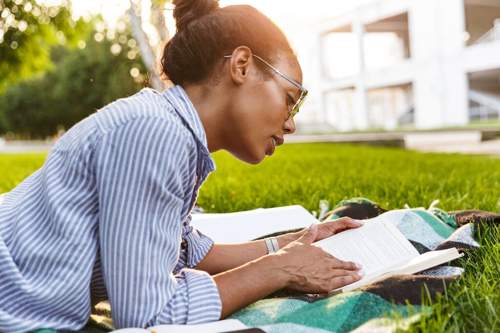 Изображение привлекательной африканской женщины, читающей книгу в парке
 - Фото, изображение