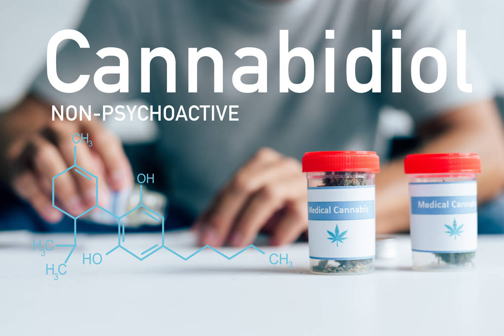 селективный фокус бутылок с медицинской марихуаной на столе с мужчиной на заднем плане с непсихоактивной иллюстрацией CBD
 - Фото, изображение
