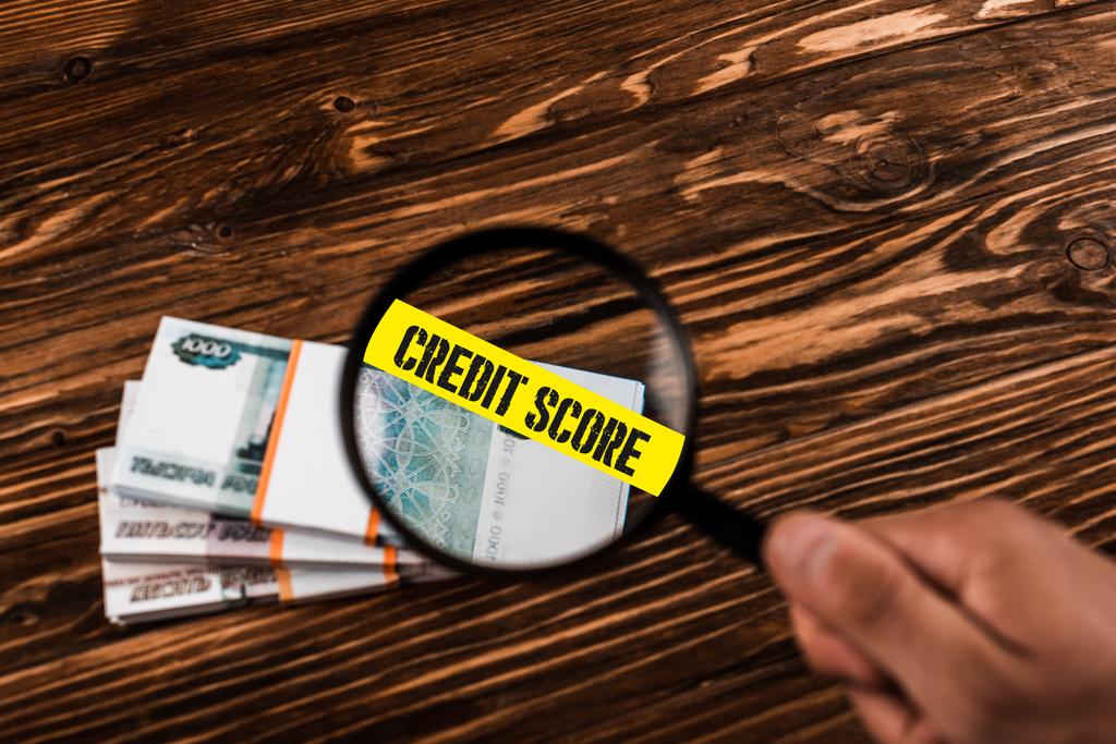 обрезанный вид человека, держащего лупу рядом с российскими деньгами на деревянном столе с иллюстрацией кредитного счета
 - Фото, изображение