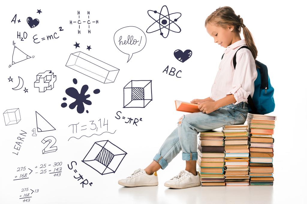 cheerful schoolkid sitting on books and reading near letters and mathematical formulas  on white  - 写真・画像