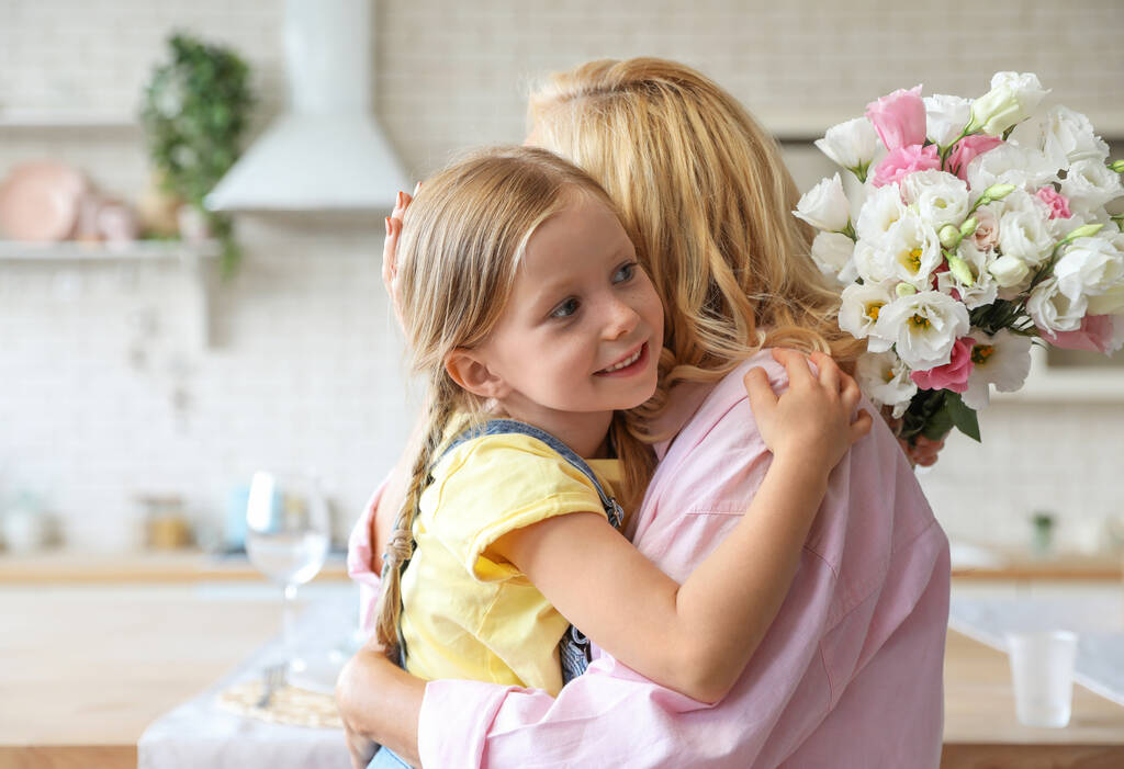 Милая маленькая девочка с букетом, обнимающая свою бабушку на кухне. Пространство для текста
 - Фото, изображение