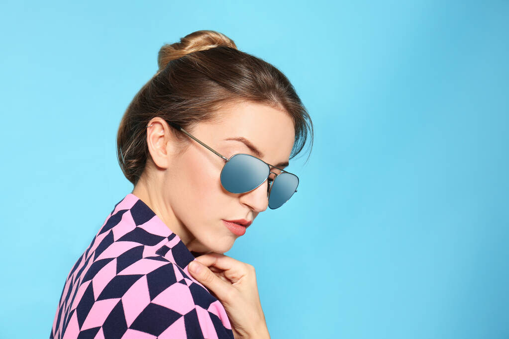 Młoda kobieta w stylowych okularach przeciwsłonecznych na niebieskim tle. Miejsce na tekst - Zdjęcie, obraz
