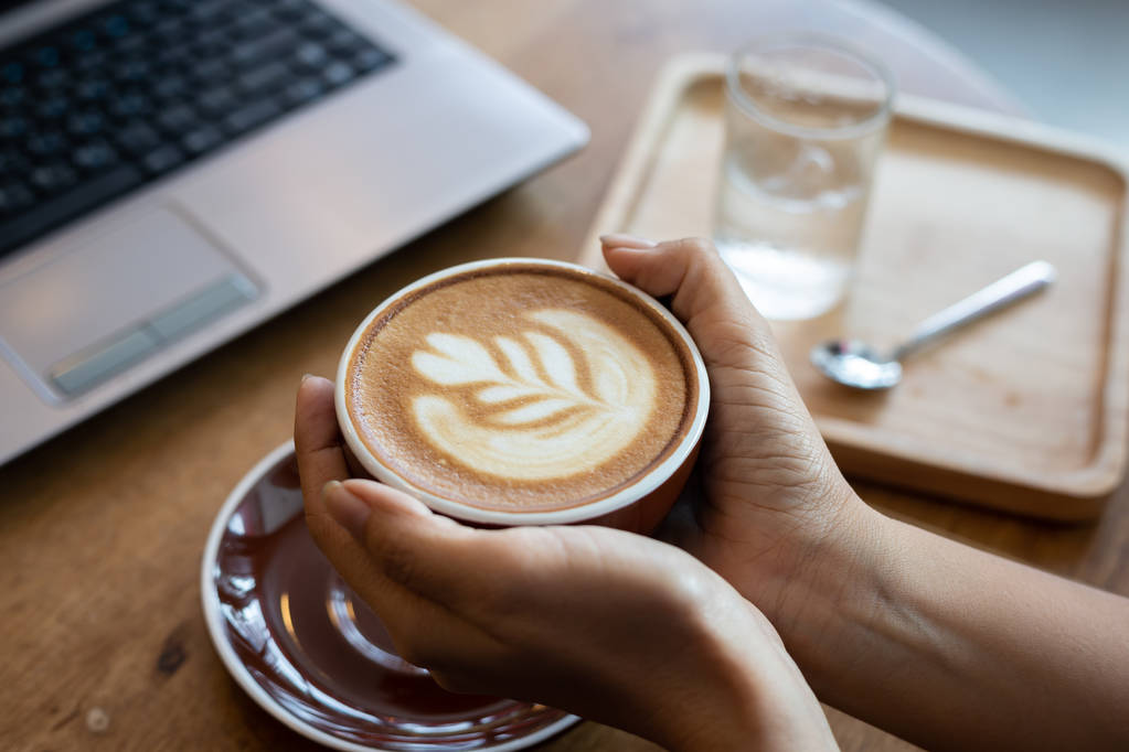 Жінка рука тримає чашку кавового латте мистецтва в кафе
. - Фото, зображення