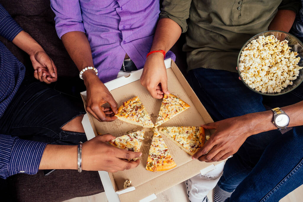 vier afrikaanse amerikaanse mannetjes eten pizza thuis feest, gooien popcorn in elkaar - Foto, afbeelding