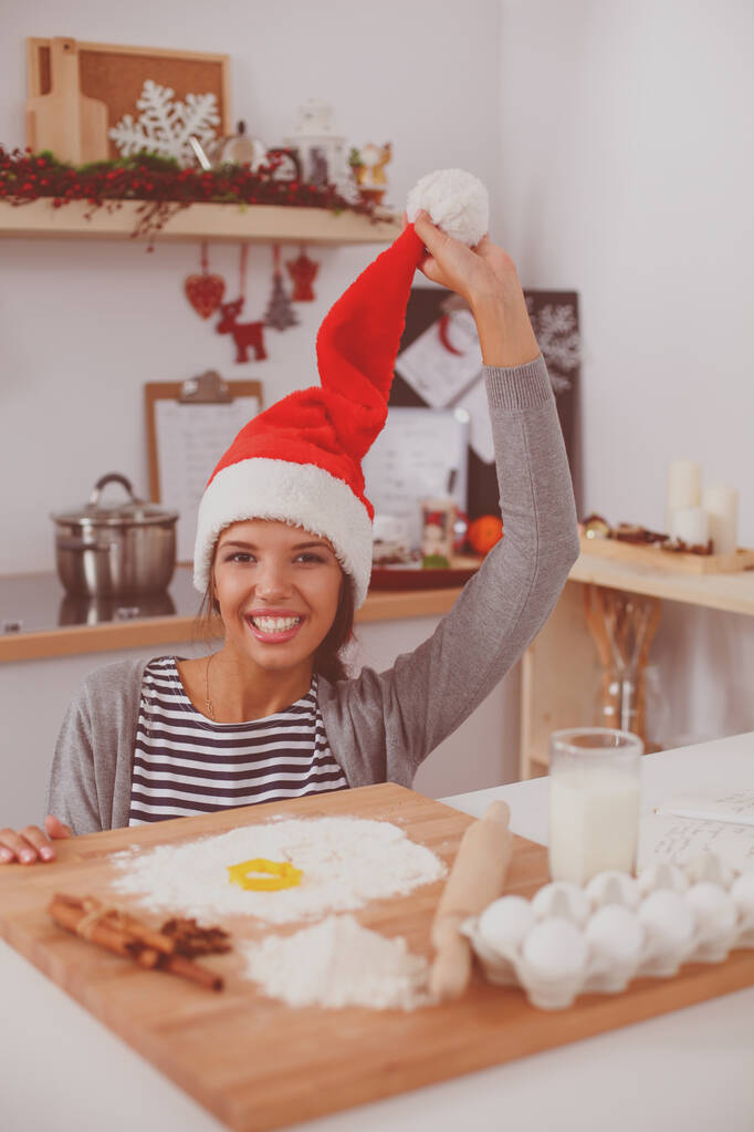 Femme au chapeau de Père Noël faire des biscuits de Noël dans la cuisine - Photo, image