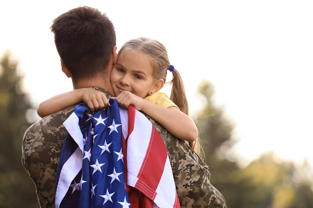Vater in Militäruniform mit amerikanischer Flagge und Tochter im sonnigen Park - Foto, Bild