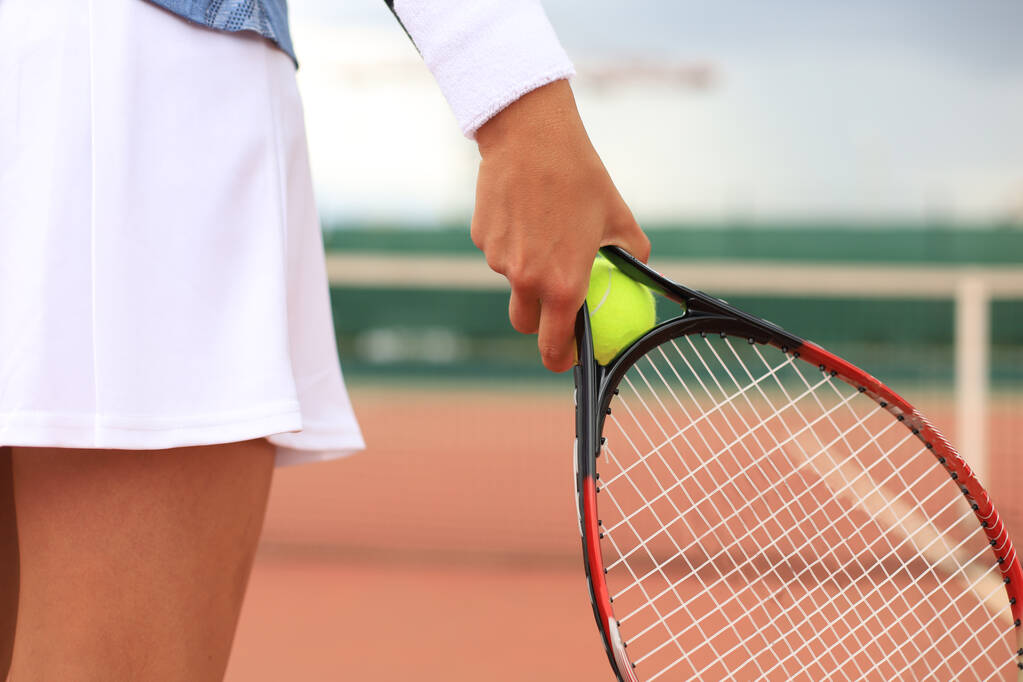 女性のクローズアップはハードテニスコートでテニスラケットを保持しています。テニスボール・イン・プレイヤーハンド. - 写真・画像