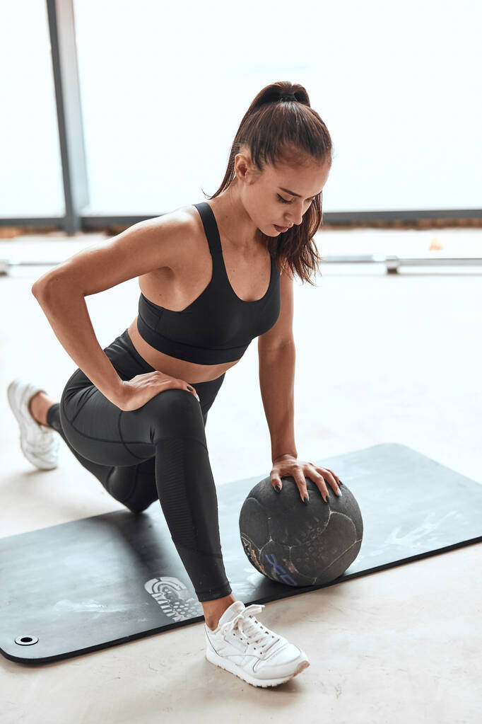 Sport lifestyle. Fit woman in sportsuit stretching legs with medicine ball at gym - Photo, Image