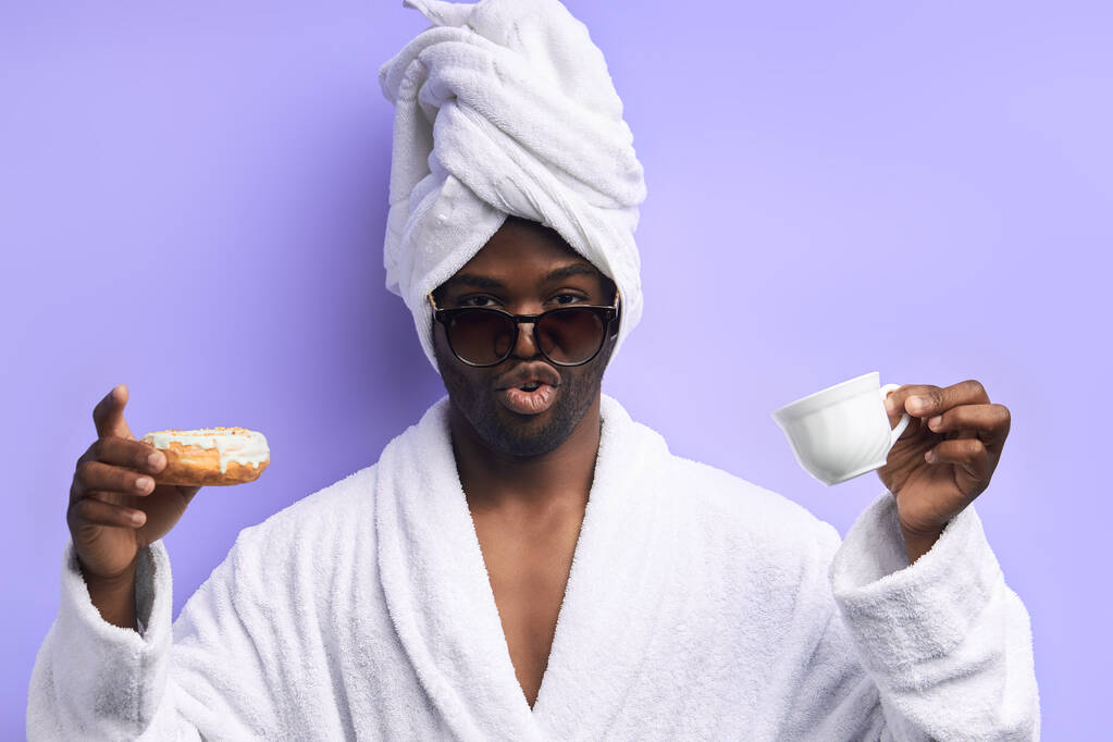 aufgeregter junger afrikanischer Mann mit glasiertem Donut und einer Tasse Tee oder Kaffee - Foto, Bild