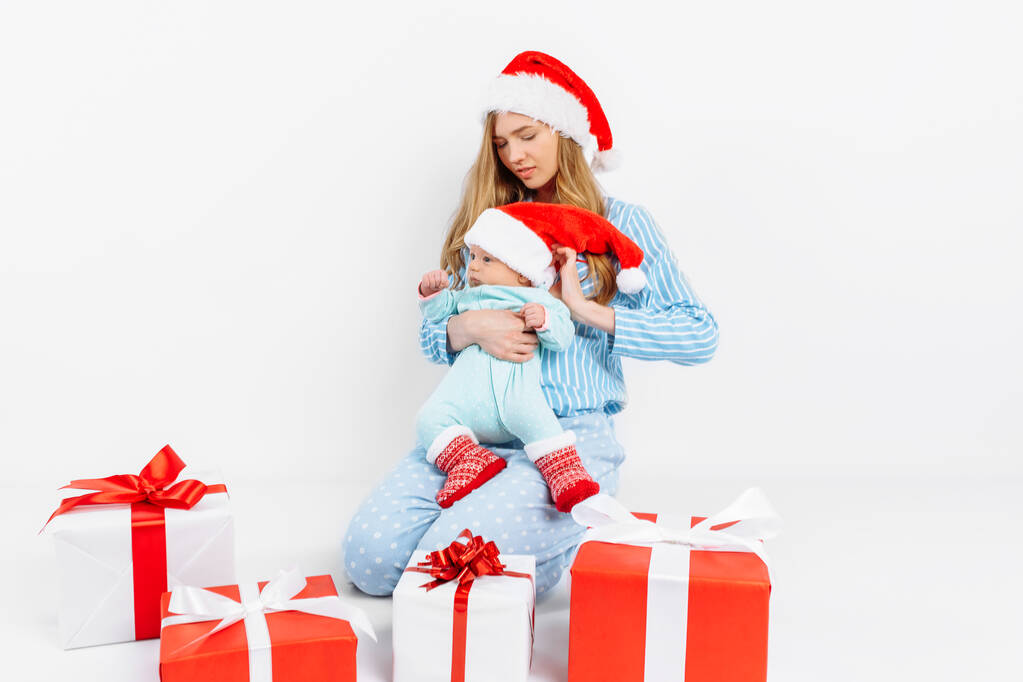 Nuori äiti antaa joulupäivänä lahjan vastasyntyneelle lapselle, tyttö pitää vauvaa sylissään joululahjalla.
 - Valokuva, kuva