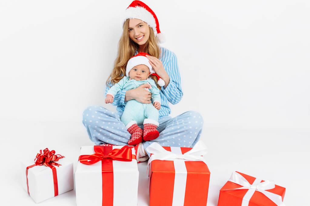 Egy fiatal anya, karácsony napján ajándékot ad egy újszülöttnek, egy lány a karjaiban tart egy babát egy karácsonyi ajándékkal. - Fotó, kép