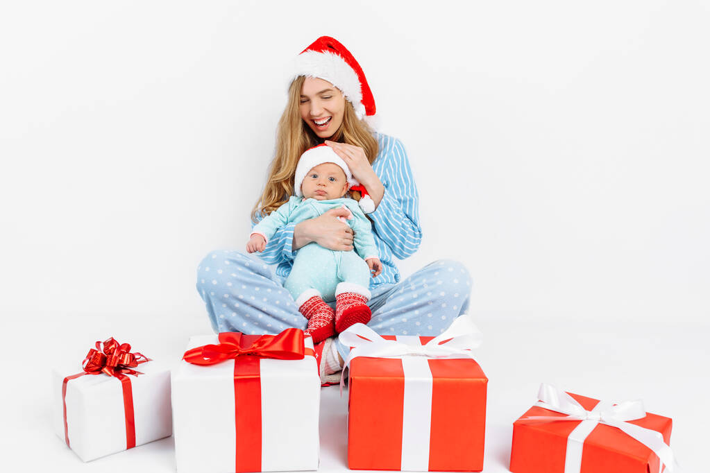 Молода мама в різдвяний день дарує подарунок новонародженій дитині, дівчинка тримає дитину в руках з різдвяним подарунком.
 - Фото, зображення