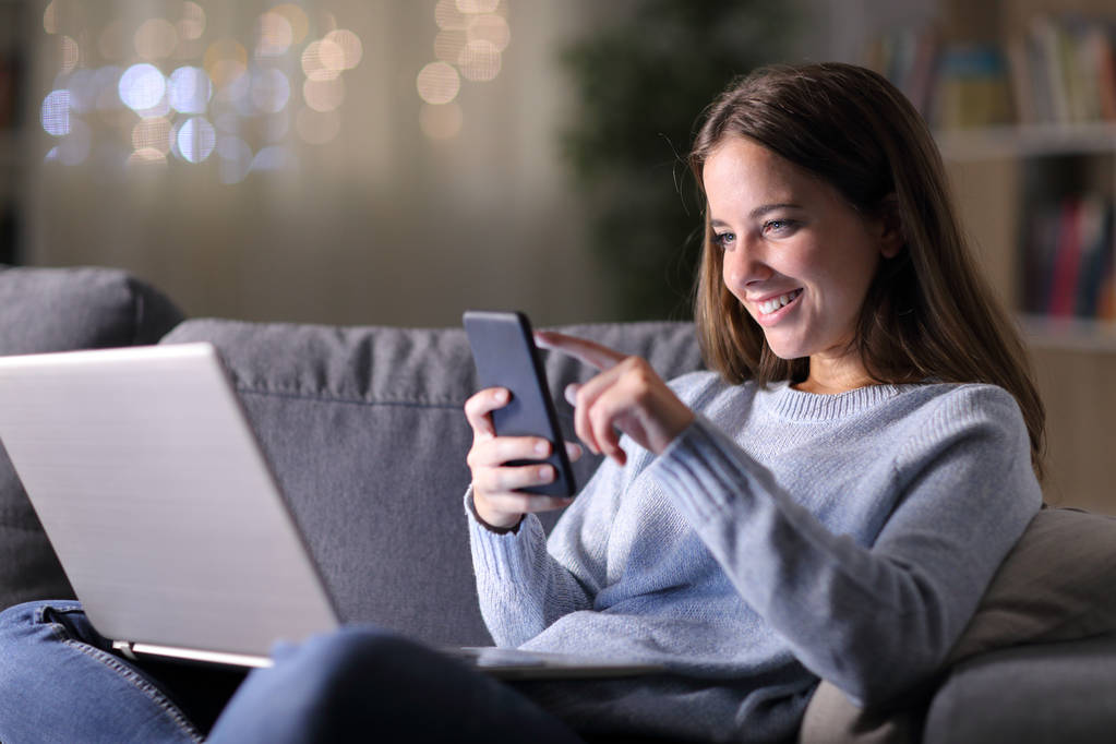 Ευτυχισμένη γυναίκα που χρησιμοποιεί φορητό υπολογιστή ελέγχει έξυπνο τηλέφωνο - Φωτογραφία, εικόνα