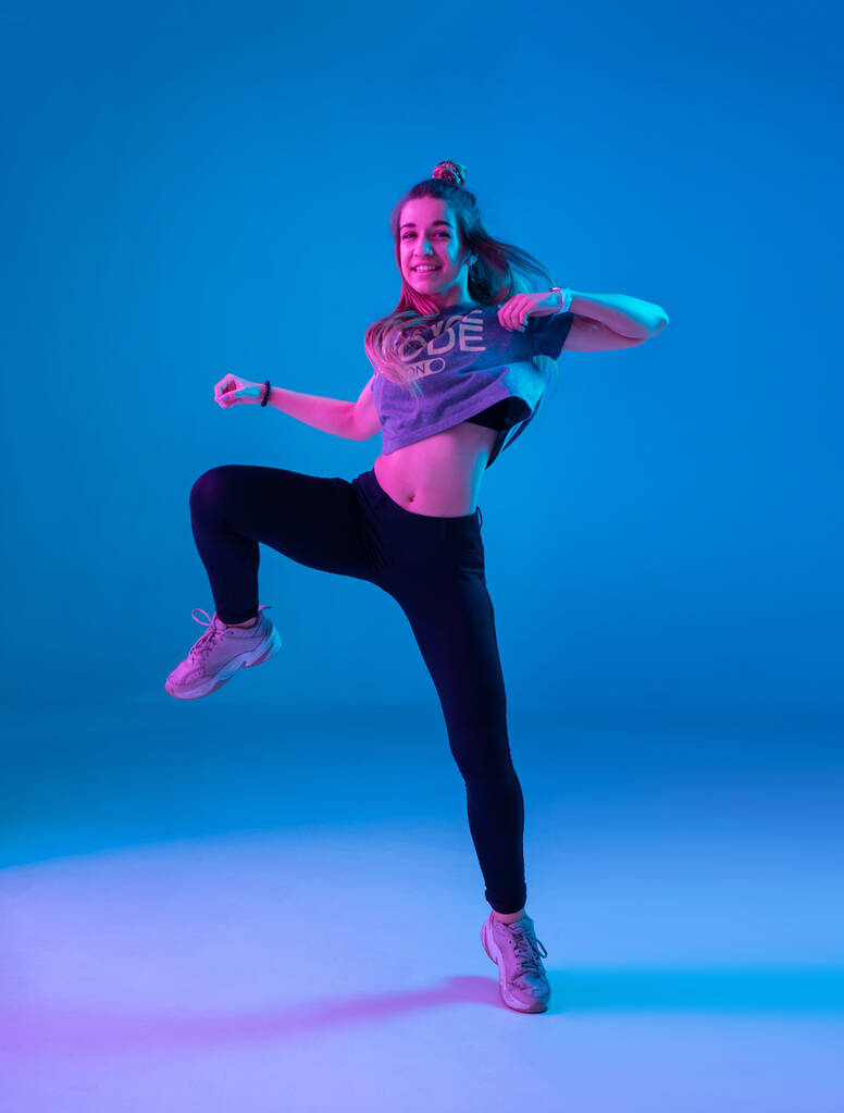 Chica joven y elegante bailando zumba en el estudio sobre un fondo de neón de color. Diseño de cartel de danza
. - Foto, imagen