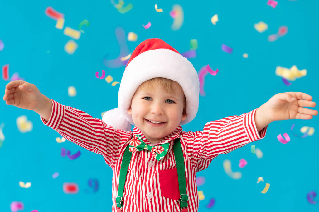 fröhliches Kind mit Weihnachtsmann-Hut vor blauem Hintergrund - Foto, Bild