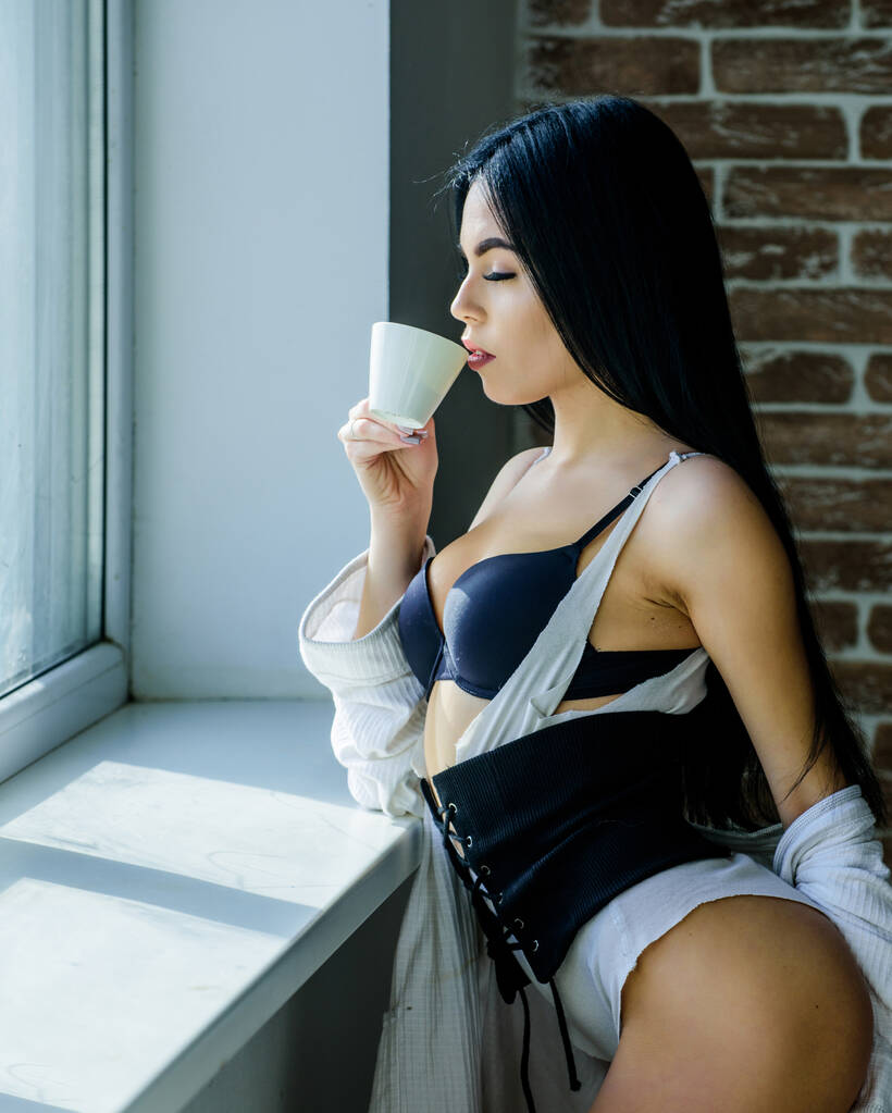 完璧なコーヒータイムだでも最初のコーヒー静けさと平和。クリーミーなカプチーノを飲みます。朝の儀式女の子の完璧な曲線ボディは窓辺のコーヒーを飲む。自宅でリラックス下着の女性 - 写真・画像