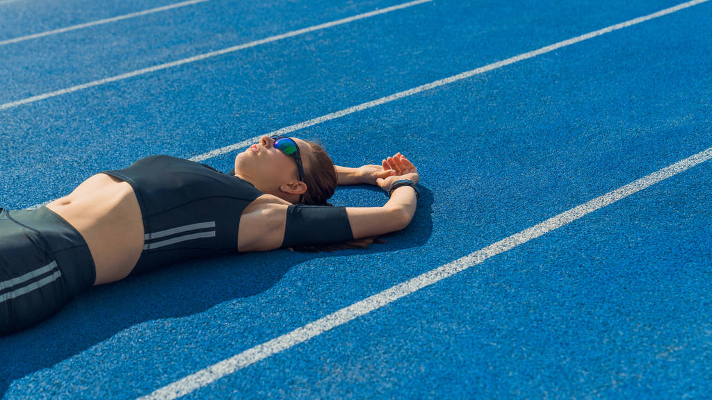 Woman athlete lying on the running track relaxing after workout. Female sprinter resting after workout lying on track on a sunny day. - Photo, Image