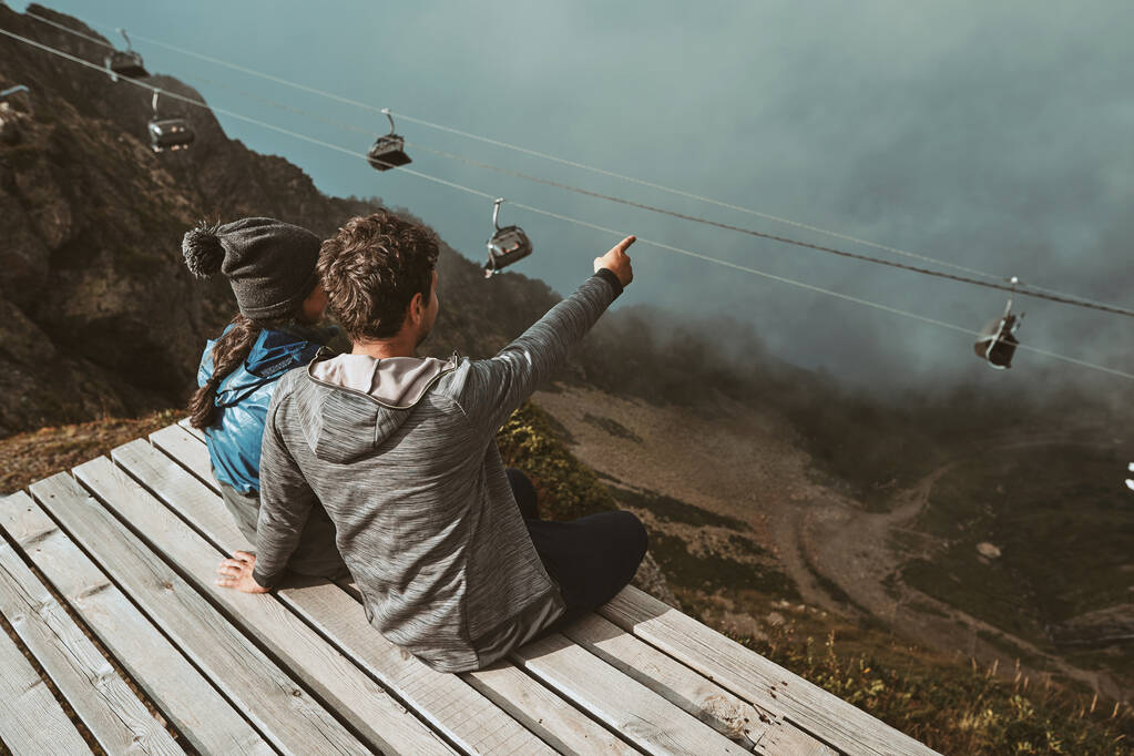 Un jeune randonneur assis en haut dans les montagnes embrassant et regardant les nuages
 - Photo, image