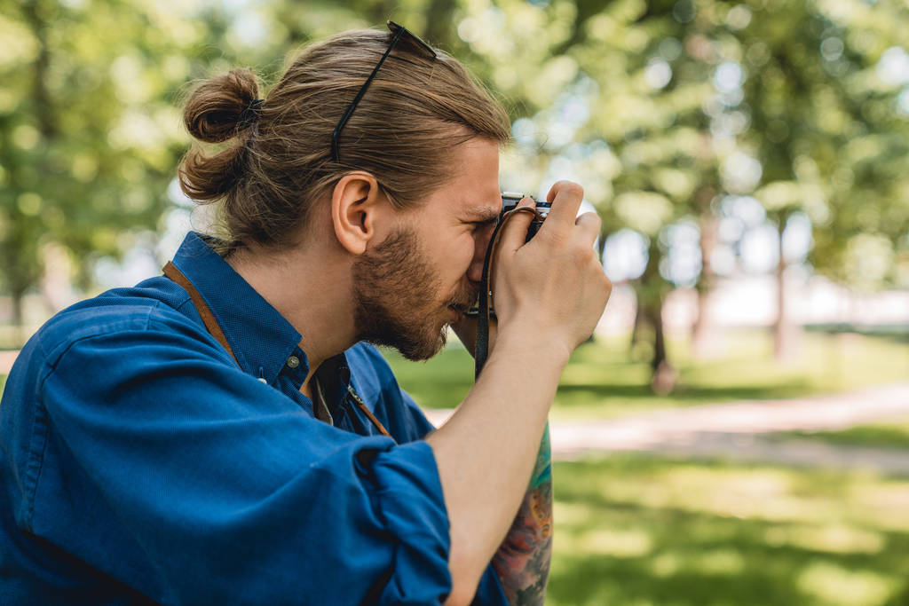 junger Mann in legerer Kleidung fotografiert die Aussicht, während er im Stadtpark im Freien steht - Foto, Bild