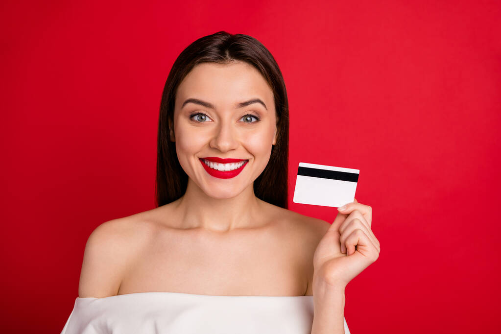 Close up zdjęcie atrakcyjnej pani z zębatym uśmiechem trzymając kartę kredytową izolowane na czerwonym tle - Zdjęcie, obraz