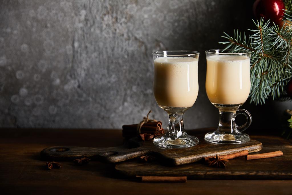 copos com deliciosa bebida eggnog na placa de corte perto do ramo de abeto no fundo de pedra cinza
 - Foto, Imagem