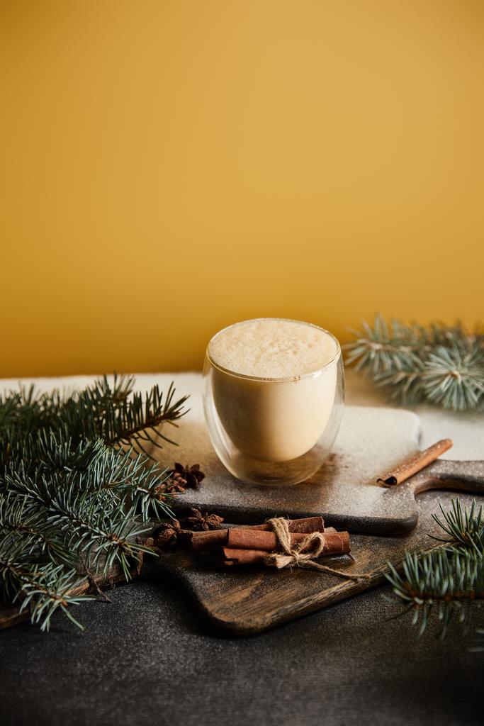 traditional eggnog cocktail on chopping board covered with sugar powder, spruce branches and cinnamon sticks on orange background - Photo, Image