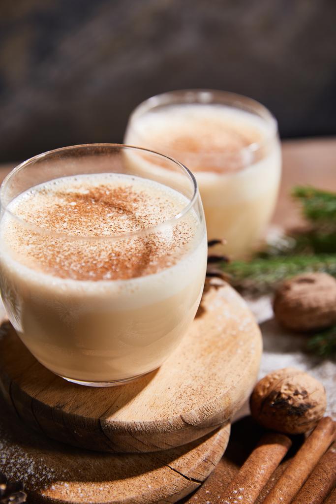 close up view of delicious eggnog cocktail on round boards, cinnamon sticks and walnuts on wooden table - Photo, Image