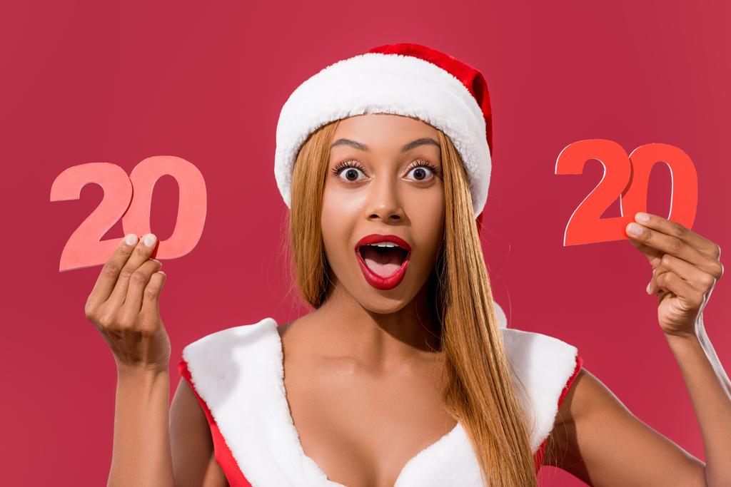 izgatott afro-amerikai lány télapó kalap és karácsonyi ruha gazdaság 2020 papír vágott szám elszigetelt piros - Fotó, kép