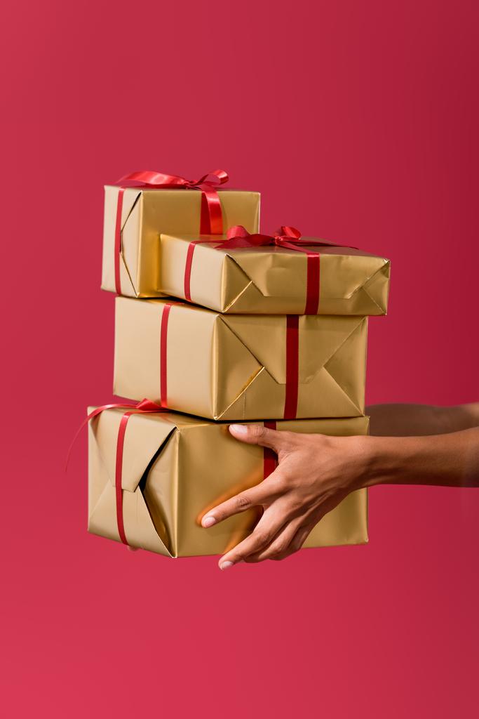 cropped view of african american woman holding gift boxes isolated on red - 写真・画像